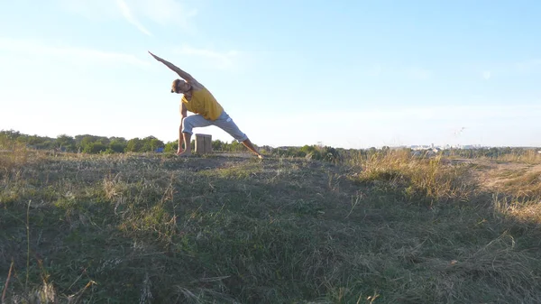 Sportieve jongeman permanent op yoga pose buiten. Kaukasische guy beoefenen van yoga beweegt en posities in de natuur. Atleet balanceren. Mooi landschap als achtergrond. Gezonde actieve levensstijl — Stockfoto