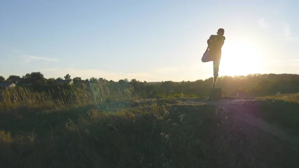 Yogi, der Yoga-Bewegungen und Positionen in der Natur praktiziert. Silhouette eines sportlichen Mannes, der beim Yoga im Freien steht. Sportler balanciert auf einem Bein. schöner Himmel und Sonne als Hintergrund. Gesunder aktiver Lebensstil — Stockfoto