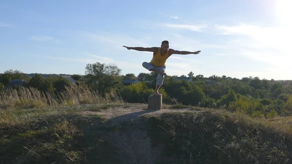 Молодой спортсмен стоит в позе йоги на открытом воздухе. Кавказский парень практикует йогу движения и позиции в природе. Йоги балансирует на одной ноге. Пейзаж как фон. Здоровый активный образ жизни — стоковое фото