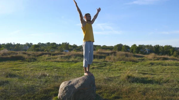 Młody człowiek sportowy znajdował się w jogi odkryty kamień. Yogi praktykowania jogi przenosi i pozycje w przyrodzie. Sportowiec równoważenia na jednej nodze. Piękny krajobraz w tle. Zdrowy, aktywny tryb życia — Zdjęcie stockowe
