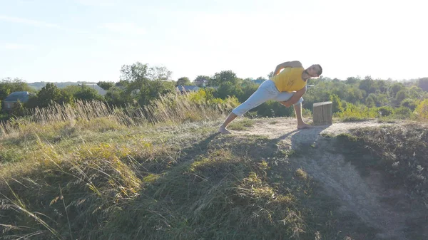 Adam pratik yoga hamle ve açık havada konumlandırır. Ayakta yoga poz, doğa, genç adam. Hill gücü egzersiz yaparak atlet. Güzel gökyüzü güneş arka plan ile. Sağlıklı aktif yaşam tarzı.