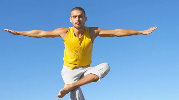Portré fiatal sportos férfi állt fa jóga póz a kék ég háttér. Kaukázusi srác jóga mozog, és a természetben pozíciók. Sportoló kiegyensúlyozó egyik lábát. Egészséges és aktív életmód — Stock Fotó