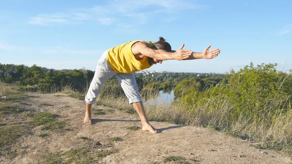 Fiatal sportos férfi állandó szabadtéri jóga póz. Kaukázusi srác jóga mozog, és a természetben pozíciók. Gyönyörű táj, mint háttér. Egészséges és aktív életmód — Stock Fotó