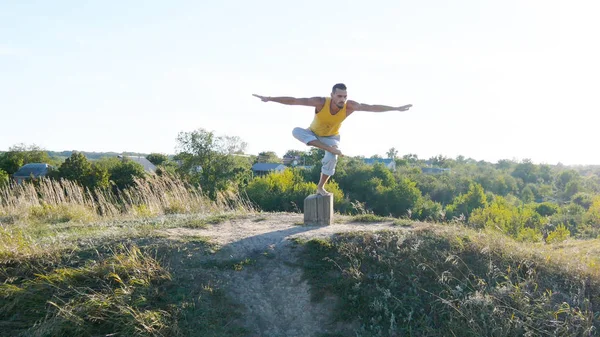 Ung sporty mand stående ved yoga positur udendørs. Kaukasiske fyr praktiserer yoga bevægelser og positioner i naturen. Yogi balancerer på et ben. Smukt landskab som baggrund. Sund aktiv livsstil - Stock-foto