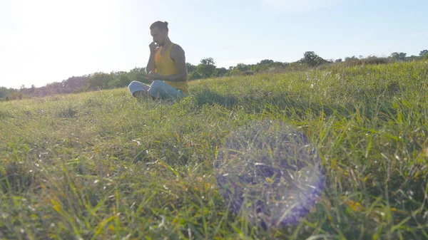 Joven sentado en yoga posan en la hierba verde en el prado y medita. Musculoso chico relajante en la pose de loto en la naturaleza. Recreación al aire libre en el día soleado. Hermoso paisaje de fondo. De cerca. —  Fotos de Stock