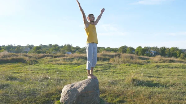Спортивний юнак стоять біля каменя на йога поза відкритий. Йоги практика йоги рухається, так і в природі. Спортсмен, балансуючи на одну ногу. Красивий краєвид як фон. Здорового активного способу життя — стокове фото