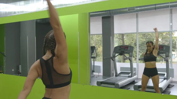 Mujer entrenando frente al espejo en el gimnasio. Atleta femenina estirando su cuerpo y manos antes del entrenamiento. Ejercitantes de chicas en el gimnasio. De cerca. —  Fotos de Stock