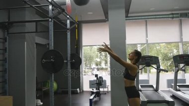 Güçlü olan kadın mükemmel fitness vücut içinde spor salonunda sağlık topu ile egzersiz. CrossFit eğitim yaparken kız. Kadın atlet egzersiz sırasında kapalı ağız kavgası. Ağır çekim. Yakın çekim