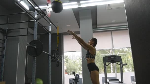 Mujer joven y fuerte con un cuerpo de fitness perfecto en ropa deportiva haciendo ejercicio con balón de medicina en el gimnasio. Chica haciendo entrenamiento crossfit. Atleta hembra sentadillas durante el entrenamiento en interiores. En cámara lenta. De cerca. — Vídeo de stock