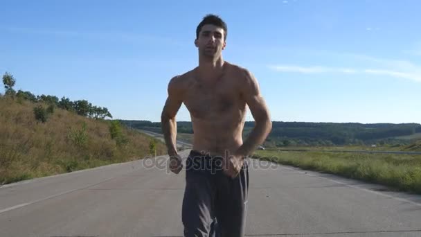 Un corredor corriendo trotando en la autopista. Deportista masculino entrenando al aire libre en verano. Joven chico musculoso fuerte haciendo ejercicio en la carretera rural durante el entrenamiento. Estilo de vida saludable activo afuera. De cerca. — Vídeos de Stock