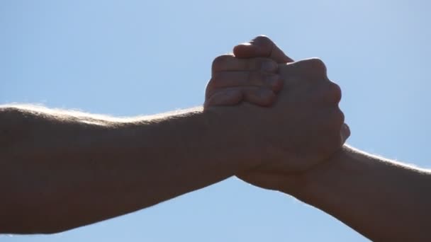 青い空を背景に 2 つの認識できない筋白人男性の友好的な握手。屋外男性腕の揺れ。外の固い握手を持つ 2 つの強い男性。チームワークと友情。クローズ アップ — ストック動画