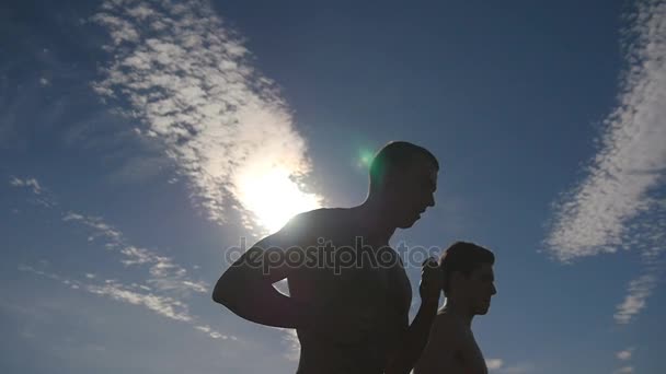 Silueta muže běhat v zemi na západ slunce. Dva mužské kondiční výcvik pro Maratonský běh. Sportovci, cvičení a běh proti modré obloze. Zdravý aktivní sportovní venkovní životní styl. Slowmotion — Stock video