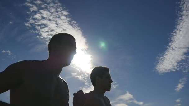 Silhuetten av män jogging i landet vid solnedgång. Två manliga jogger utbildning för marathon kör. Idrottare tränar och kör mot blå himmel. Hälsosam aktiv sport utomhus livsstil. Slowmotion — Stockvideo