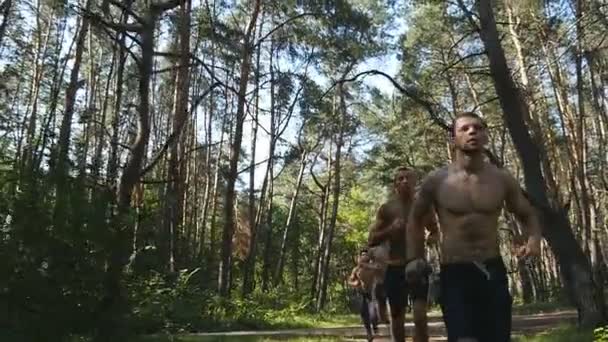 Группа молодых мускулистых спортсменов бежит по лесной тропе. Подходящие атлетичные спортсмены мужского пола тренируются. Люди тренируются и тренируются. Спортивные люди бегут по лесу. Медленное движение — стоковое видео