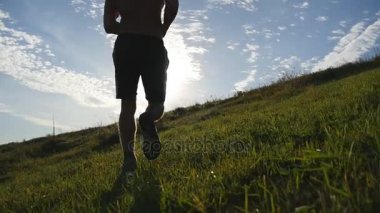 Mavi gökyüzü arka plan üzerinde yeşil tepeden koşan genç adam. Erkek atlet doğada günbatımında koşu. Koşu spor atlet açık parlama ile gündoğumu, yokuş yukarı. İkinci el eğitim. Ağır çekim