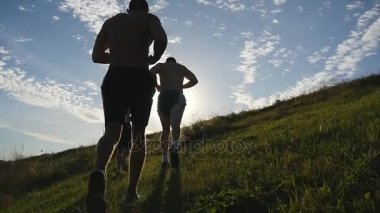 Yeşil tepenin üzerinde mavi gökyüzü arka plan üzerinde çalışan genç erkekler. Erkek sporcular günbatımında doğada yürüyüş. Spor yokuş yukarı koşu koşucular gündoğumu parlama ile açık. İkinci el eğitim. Slowmotion