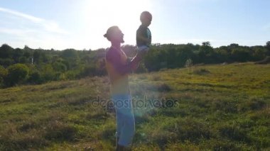 Doğa onun çocuğuna oynayan genç baba. Baba oğlu holding bacaklar ve açık atar. Mutlu bir aile birlikte dışarıda çayır vakit. Arka plan, güzel manzara. Yakın çekim