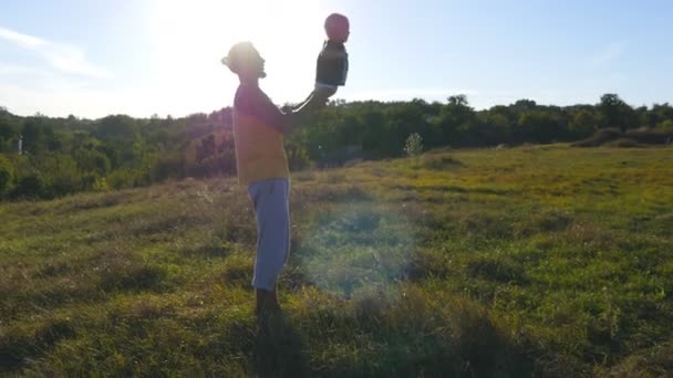 Joven padre jugando con su hijo en la naturaleza. Papá sostiene las piernas de sus hijos y las lanza al aire libre. Feliz familia pasando tiempo juntos afuera en el prado. Hermoso paisaje de fondo. De cerca. — Vídeos de Stock