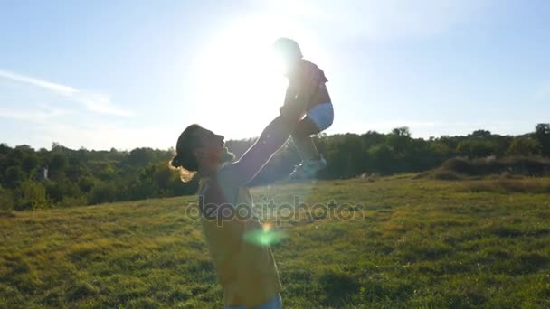Молодой отец играет со своим маленьким сыном на открытом воздухе. Папа поднимает своего ребенка на природе. Счастливая семья проводит время вместе на лугу. Красивый пейзаж на заднем плане. Закрыть — стоковое видео