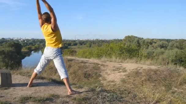 Young sporty man standing at yoga pose outdoor. Caucasian guy practicing yoga moves and positions in nature. Beautiful landscape as background. Healthy active lifestyle — Stock Video