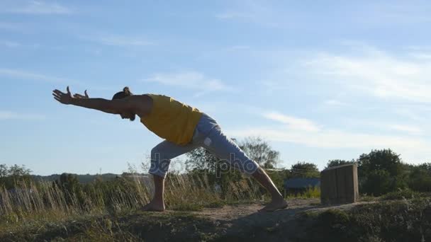 Kille öva yoga flyttar och positioner utomhus. Ung man stående på yogaställning på naturen. Idrottsman gör styrka träning på kullen. Landskap i bakgrunden. Hälsosam aktiv livsstil. Närbild — Stockvideo