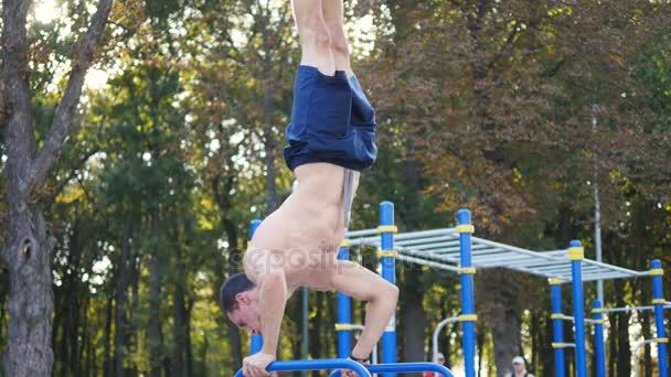 Güçlü kas adam amuda bir parkta. Kaslı erkek spor adamı yatay çubuklarında açık stunts yapıyor. Sporcu eğitim kas dışında bir hareketten gerçekleştirir. Egzersiz spor yaşam tarzı — Stok video