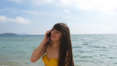 Genç çekici kadın bir mayo bir deniz plajda cep telefonunda konuşuyor. Mutlu kız cep telefonu arka plan okyanusun üzerinde konuşan bikini. Yaz tatili ara. Yakın çekim