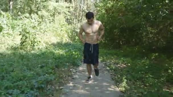 Joven atleta musculoso corriendo por el sendero del bosque. Hombre fuerte activo entrenando al aire libre. Ajuste guapos deportistas atléticos masculinos haciendo ejercicio. Guy entrenando y haciendo ejercicio. Estilo de vida saludable. De cerca. — Vídeos de Stock