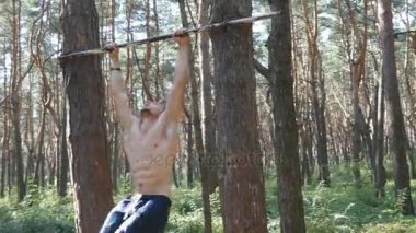 Karın egzersizleri orman yatay çubuk performans mükemmel fitness vücut atletik kaslı adam. Adam bacaklar kaldırma. Adam ahşap açık eğitim. O asılı ve yükseltir ayaklar.