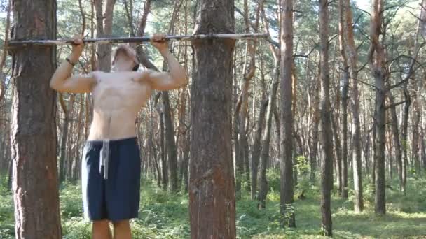 Сильный мускулистый человек, подтягивающийся в лесу. Молодой спортсмен делает подтяжки на горизонтальных брусьях в лесу. Фитнес мускулистый человек тренируется летом на открытом воздухе. Спортивные тренировки здоровый образ жизни. Закрыть — стоковое видео