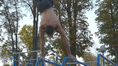 Güçlü kas adam amuda bir parkta. Kaslı erkek spor adamı yatay çubuklarında açık stunts yapıyor. Sporcu eğitim kas dışında bir hareketten gerçekleştirir. Ağır çekim