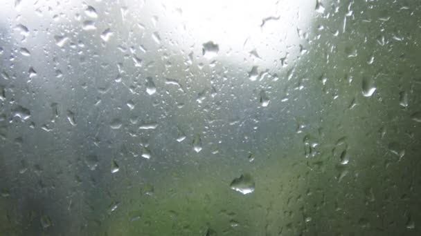 Zbliżenie: kropelki wody na szybie. Krople deszczu na oknie szkło z rozmycie tła. Niewyraźne drzewa i niebo. Deszczowe dni, deszcz, prowadzący w dół okna, bokeh — Wideo stockowe