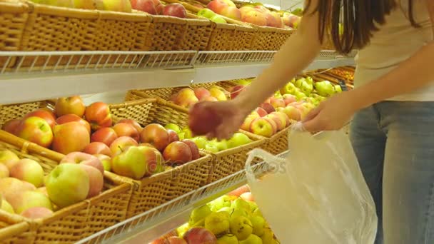 Žena výběr čerstvých červených jablek v obchodě vyrobit oddělení a umístit ho do plastového sáčku. Mladá krásná dívka je volba jablka v supermarketu a jejich vkládání do košíku — Stock video