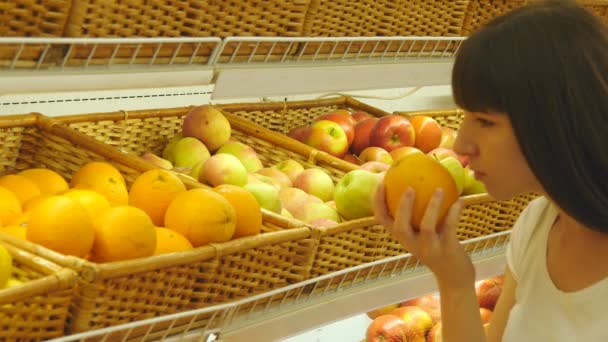 Donna che seleziona arance fresche nel reparto prodotti alimentari e lo annusa. Giovane bella ragazza sta scegliendo frutta nel supermercato — Video Stock