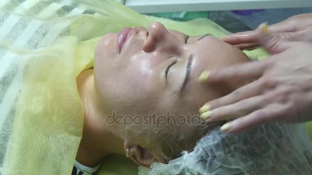 Manos de esteticista acariciando la cara del cliente. Masaje facial hermosa chica. Retrato de una joven en el salón de belleza. Cosmetólogo haciendo masaje de cara femenina. Primer plano . — Vídeo de stock