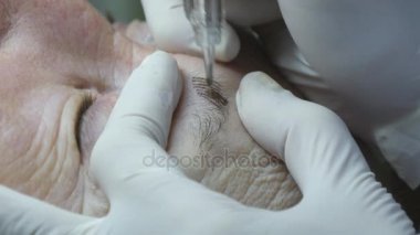 Yaşlı kadın yalan ve Başlarken kaşları makyaj Güzellik Salonu. Kalıcı hale kirpik üzerinde uygulanması. Kalıcı makyaj kirpik yapma güzellik uzmanı. Kaşları ile ana çalışır. Yarı kalıcı makyaj