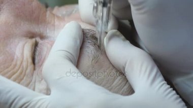 Yaşlı kadın yalan ve Başlarken kaşları makyaj Güzellik Salonu. Kalıcı hale kirpik üzerinde uygulanması. Kalıcı makyaj kirpik yapma güzellik uzmanı. Kaşları ile ana çalışır. Yarı kalıcı makyaj
