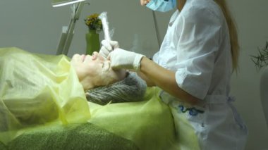 Yaşlı kadın yalan ve Başlarken kirpik makyaj Güzellik Salonu. Kalıcı hale kaslar üzerinde uygulanması. Kalıcı makyaj kirpik yapma güzellik uzmanı. Kaşları ile ana çalışır. Yarı kalıcı makyaj