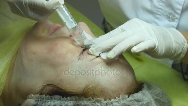 La anciana miente y consigue maquillaje de pestañas en el salón de belleza. Aplicar maquillaje permanente sobre la pestaña. Las manos del esteticista están preparando la piel para el procedimiento o la limpieza después del procedimiento. — Vídeos de Stock