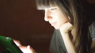 Tablet bilgisayar kanepede yatan genç kadın. Tablet bilgisayar evde gece geç saatlerde kullanan kız. Yüzünde parlayan ışık. O online alışveriş için hareket eden aygıt kullanır, sosyal medya okuma, internette surf