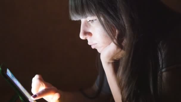 Jonge vrouw met tablet PC liggend op de Bank. Meisje met tablet pc thuis late nacht. Gloeiend licht op het gezicht. Ze maakt gebruik van mobiel apparaat tot winkelen online, sociale media lezen, surfen op het internet — Stockvideo