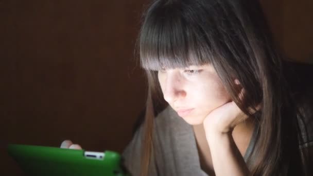 Mujer joven con Tablet PC acostado en el sofá. Chica usando tableta en casa tarde por la noche. Brillante luz en la cara. Utiliza dispositivos móviles para ir de compras en línea, leer las redes sociales, navegar por Internet — Vídeos de Stock