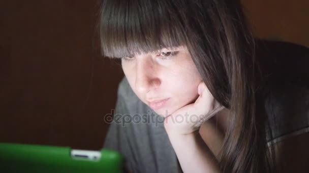 Mujer joven con Tablet PC acostado en el sofá. Chica usando tableta en casa tarde por la noche. Brillante luz en la cara. Utiliza dispositivos móviles para ir de compras en línea, leer las redes sociales, navegar por Internet — Vídeo de stock