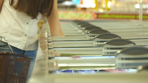 スーパー マーケットで冷凍セクションのガラスのドアを開くと、冷凍食料品の選択の女性の手。若い女性の店で冷蔵庫から商品を取って、バスケットに入れて — ストック動画