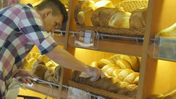 El hombre elige un pan fresco en el supermercado. Un joven toma una barra de pan de la estantería y la huele. Compras en el supermercado — Vídeos de Stock