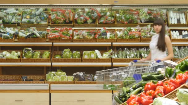 Eine junge Frau schiebt einen Einkaufswagen durch die Gänge des Supermarktes. Mädchen wählen frisches Gemüse im Supermarkt und legen es in den Einkaufswagen. Mädchen kauft Pilze im Laden — Stockvideo