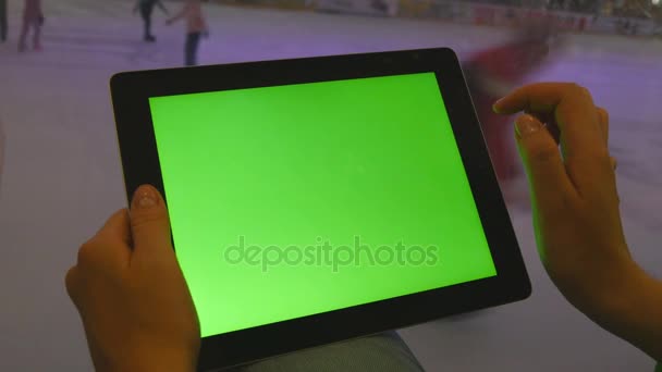 Mãos femininas usando tablet pc com tela verde no shopping center. Muitas pessoas patinam na pista de gelo interior ao fundo — Vídeo de Stock