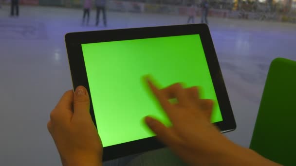 Mains féminines utilisant tablette PC avec écran vert dans le centre commercial. Beaucoup de gens patinent sur la patinoire intérieure à l'arrière-plan — Video