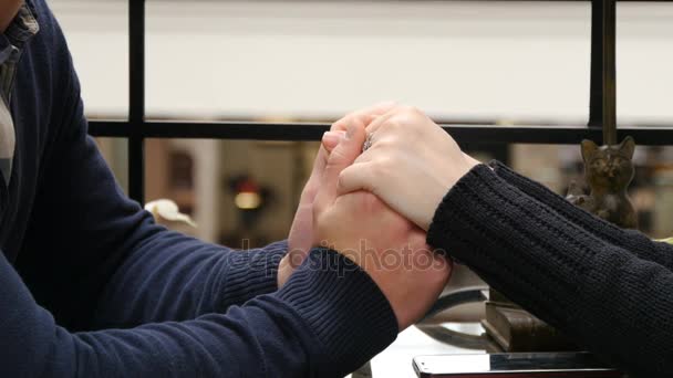 Молодий чоловік в окулярах ніжно погладжує і цілує жіночу руку. Щаслива пара тримає і торкається один одного руки в кафе в торговому центрі . — стокове відео