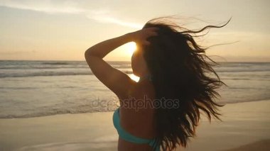 Bikini ayakta deniz günbatımı güzel genç kadın. Erkek sahilde tatil sırasında hayattan zevk. Okyanus kıyısında güneş doğarken poz uzun saçlı çekici seksi kız. Ağır çekim
